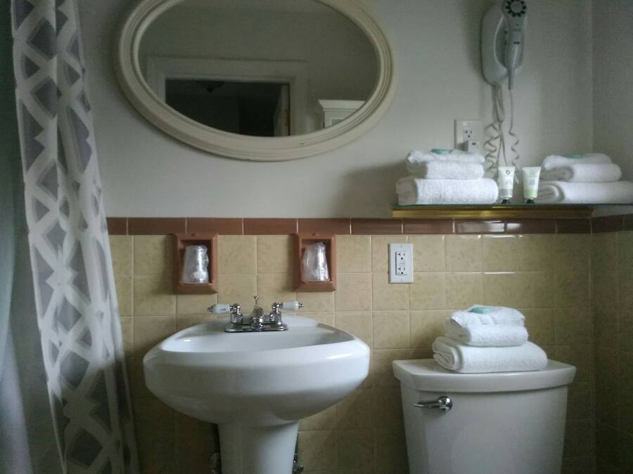 Un baño con lavamanos, inodoro y espejo. Hay toallas y artículos de aseo en la encimera.
