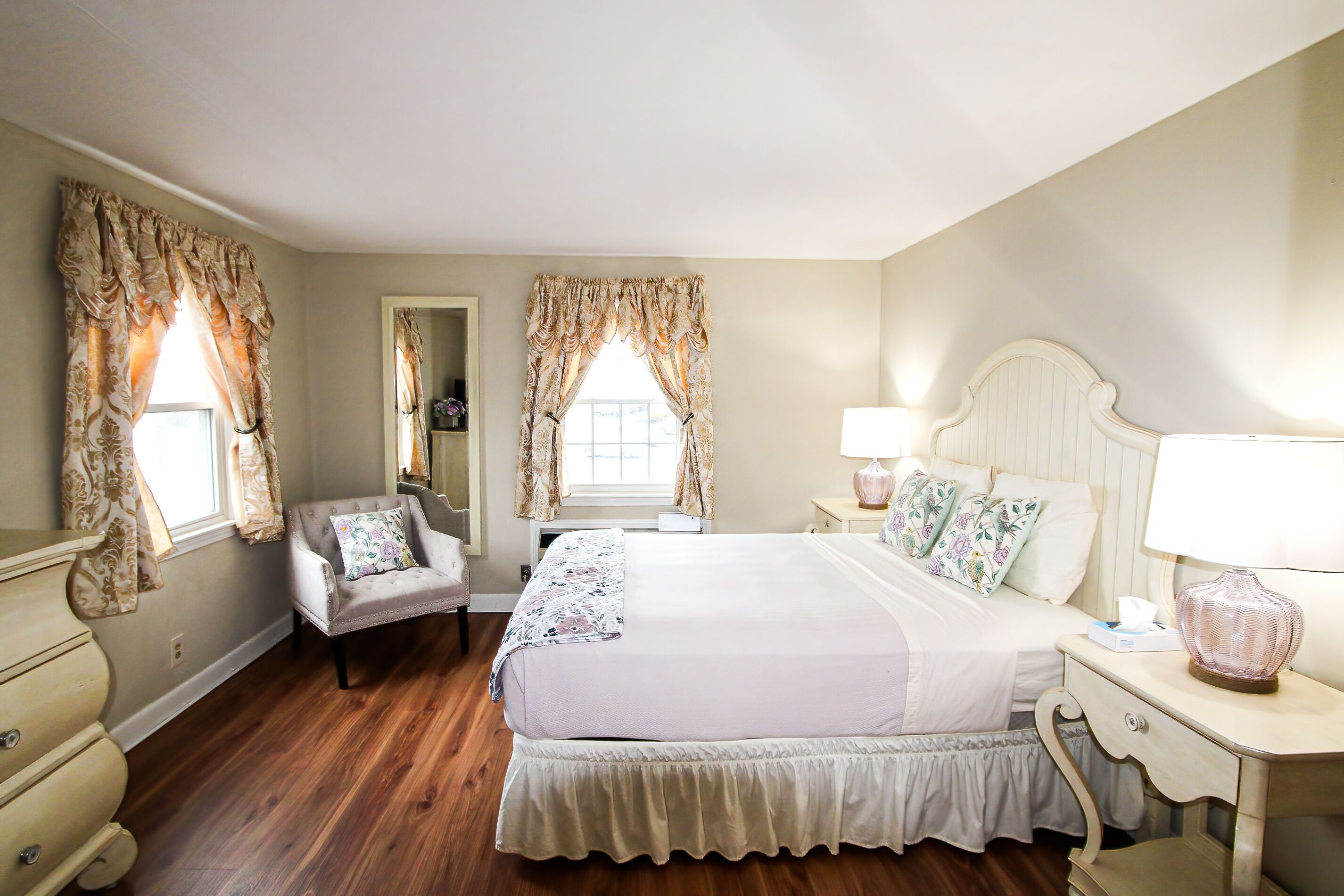 A bedroom with a large bed, two bedside tables with lamps, a chair, and curtains.