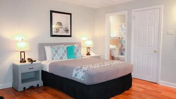 A bedroom with a bed, nightstands, a lamp, a framed picture, a door, and a bathroom visible through an open door.