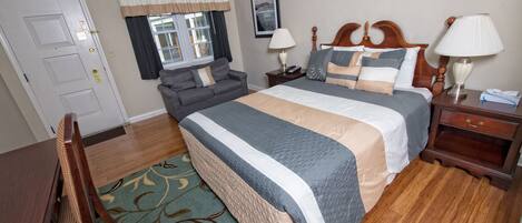 A hotel room with a large bed, a sofa, a wooden nightstand, a desk, and a chair.