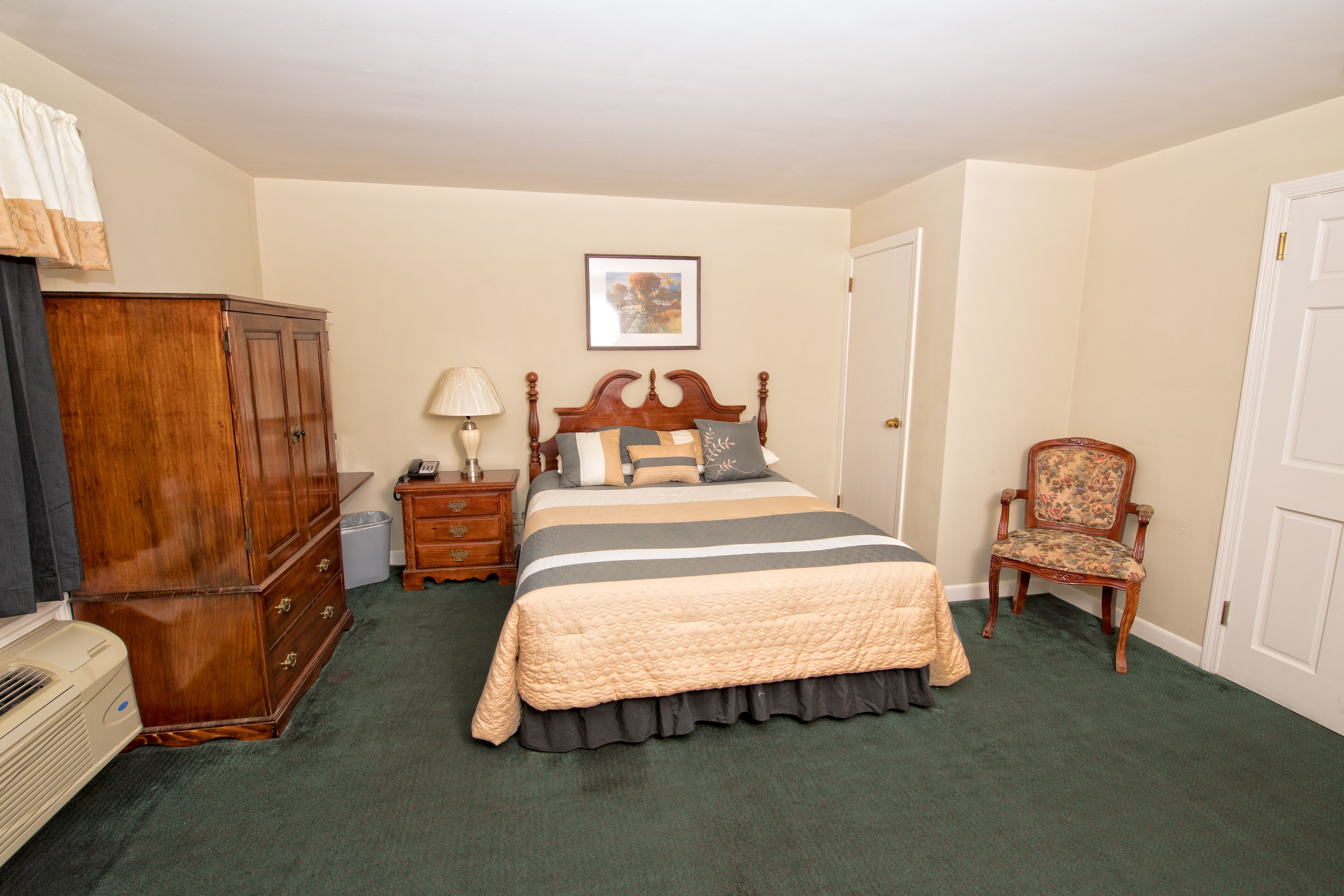 A bedroom with a large bed, a wooden wardrobe, a chair, a nightstand, and a lamp.