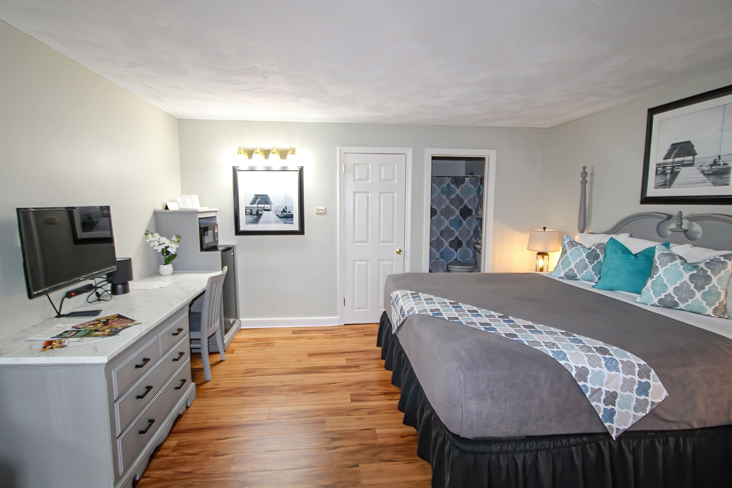 A bedroom with a bed, a desk with a TV, a dresser, and a door leading to a bathroom.