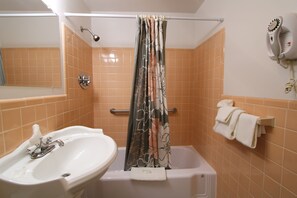 A bathroom with a sink, bathtub, shower curtain, towel rack, and a hairdryer on the wall. - Colonial Inn Seekonk (Seekonk)