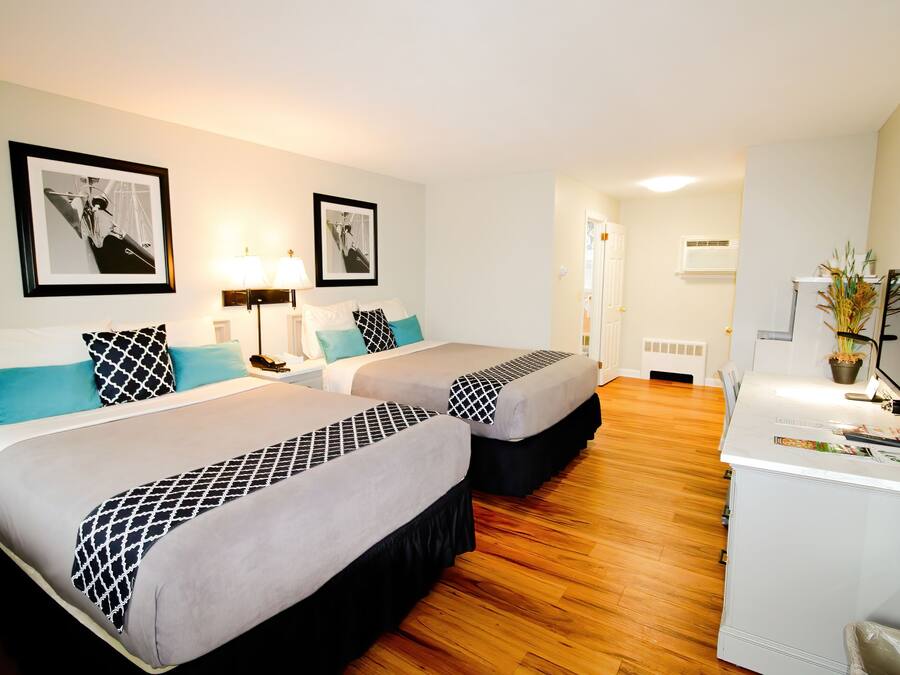 A hotel room with two beds, a desk with a computer, and framed pictures on the wall.