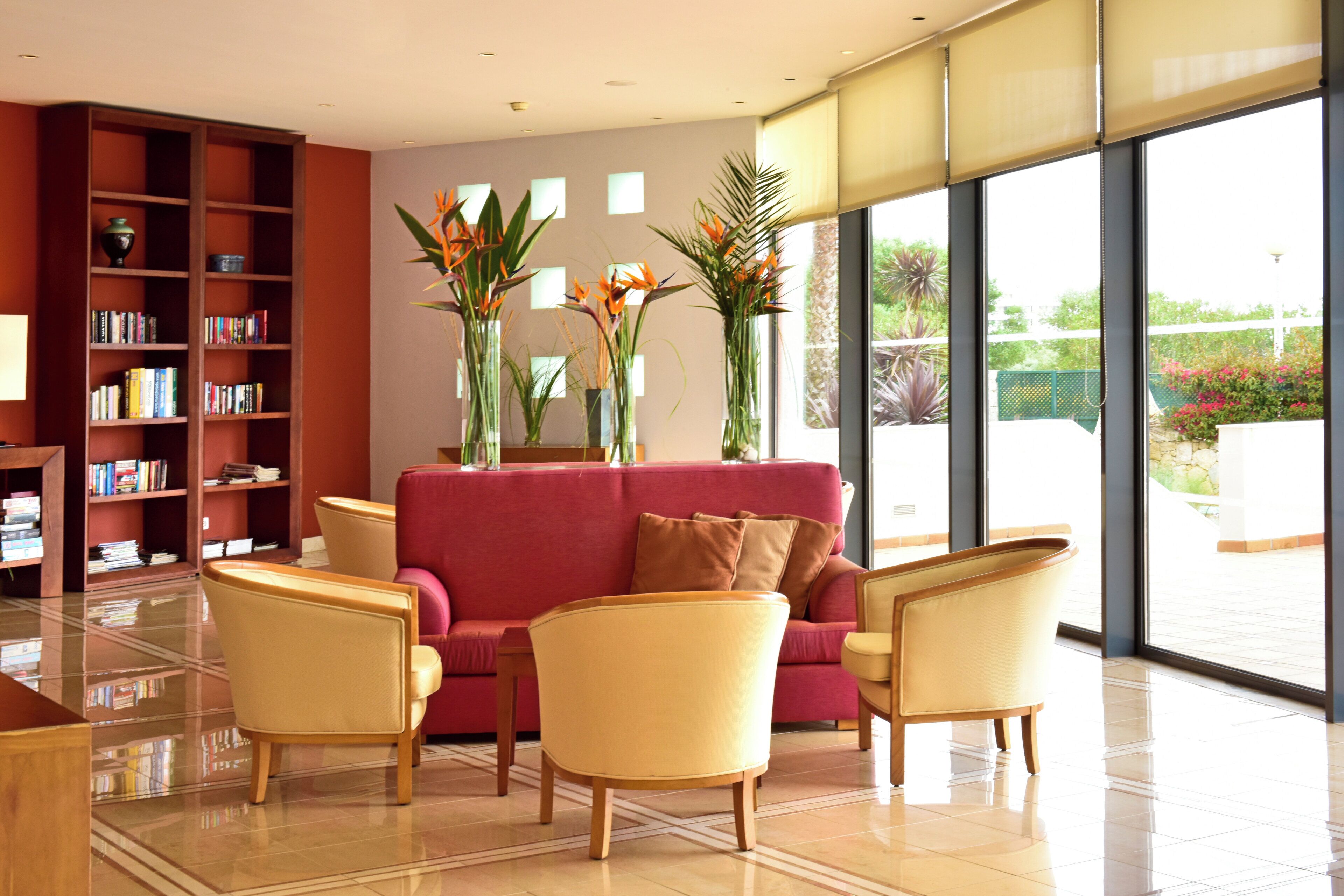 A modern interior with a red sofa, yellow chairs, a bookshelf, and large windows.