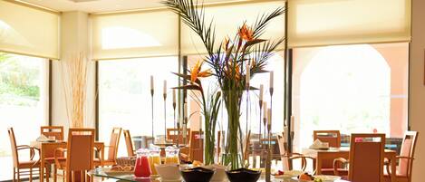 A dining area with a glass table, chairs, and a centerpiece with plants.
