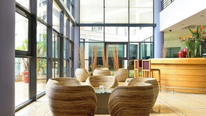 Eine moderne Lobby mit großen Fenstern, einer Rezeption und mehreren großen Sitzgelegenheiten aus gewebtem Material.