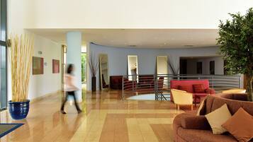 Un vestíbulo amplio con un sofá rojo, un jarrón azul con plantas altas y una escalera moderna.