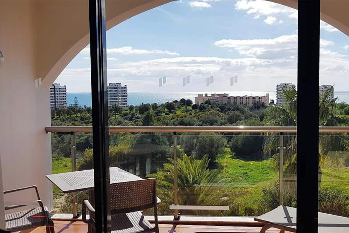 Een balkon met een tafel en stoelen, met uitzicht op een weelderig groen landschap en de kust.
