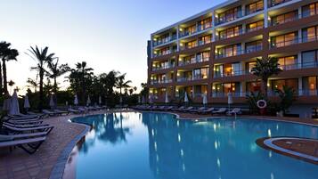 A hotel with a swimming pool, lounge chairs, and palm trees.