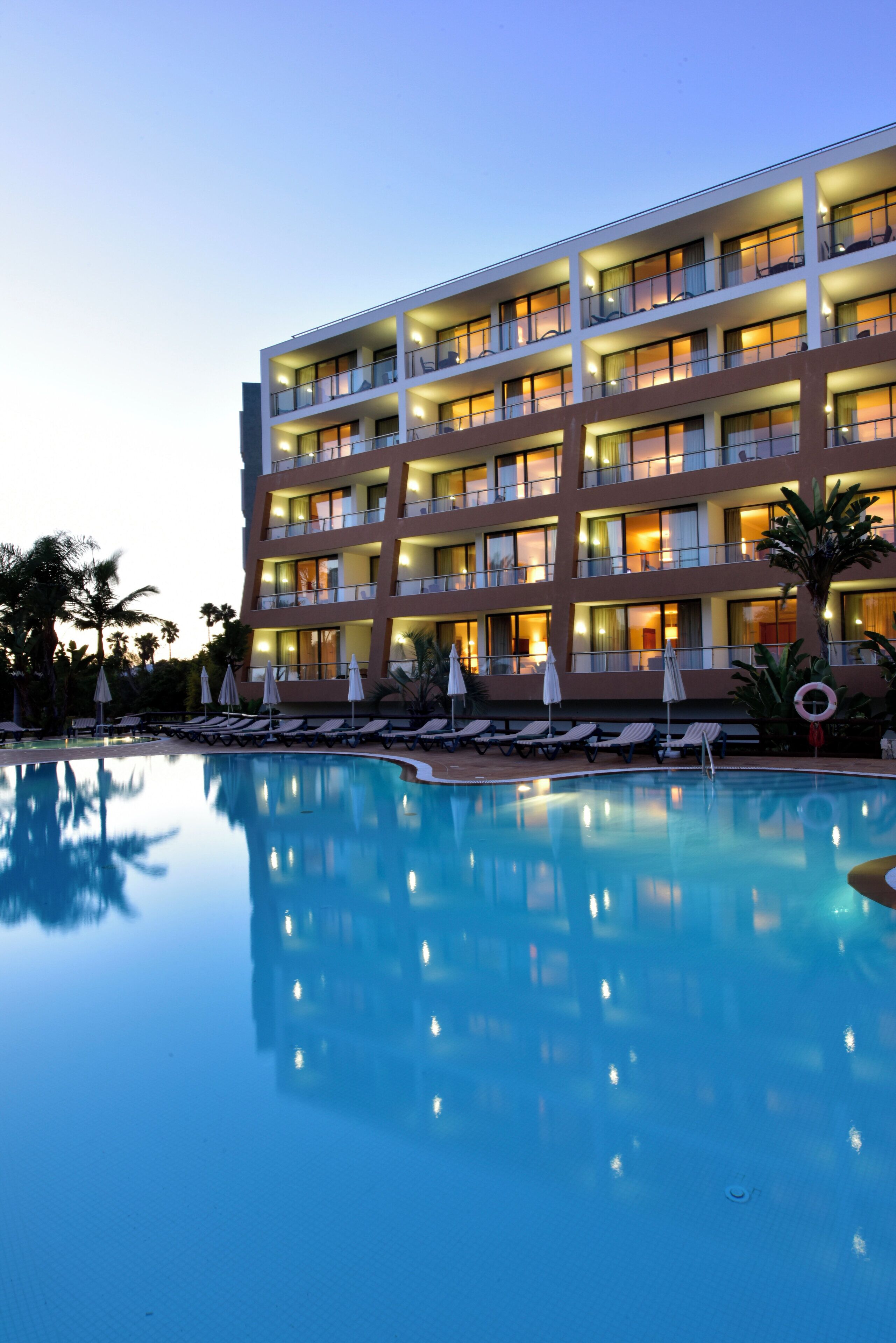 Un hôtel à plusieurs étages doté d’une piscine, de chaises longues et de parasols.