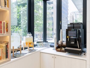 Interior de café com máquina de café, uma janela ampla e estantes de livros.
