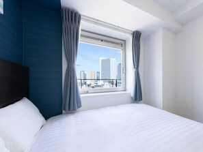 A hotel room with a large bed, a view of the cityscape through a window, and blue curtains. - Comfort Hotel Yokohama Kannai (Yokohama)