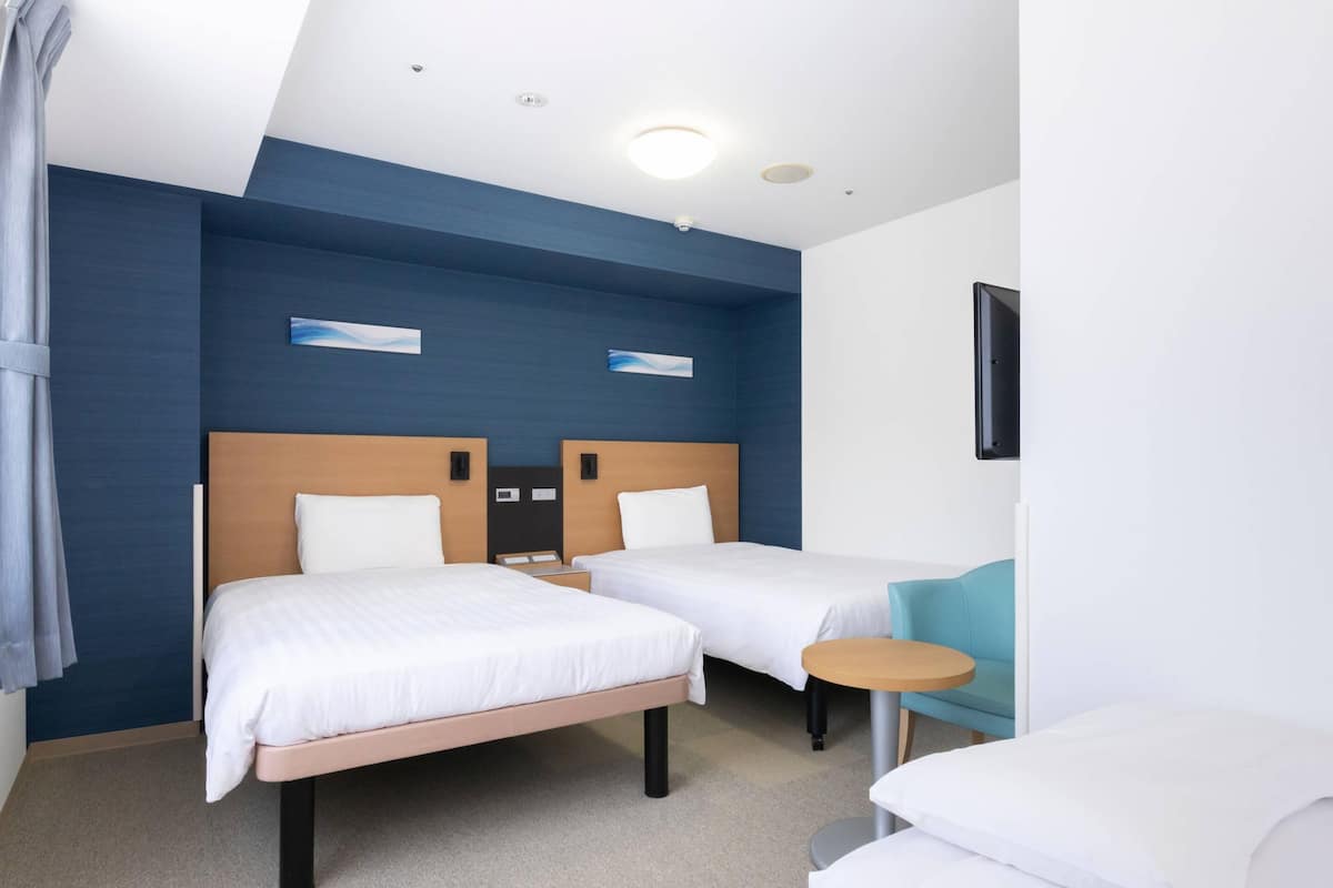 A hotel room with two beds, a small round table, and a TV mounted on the wall.