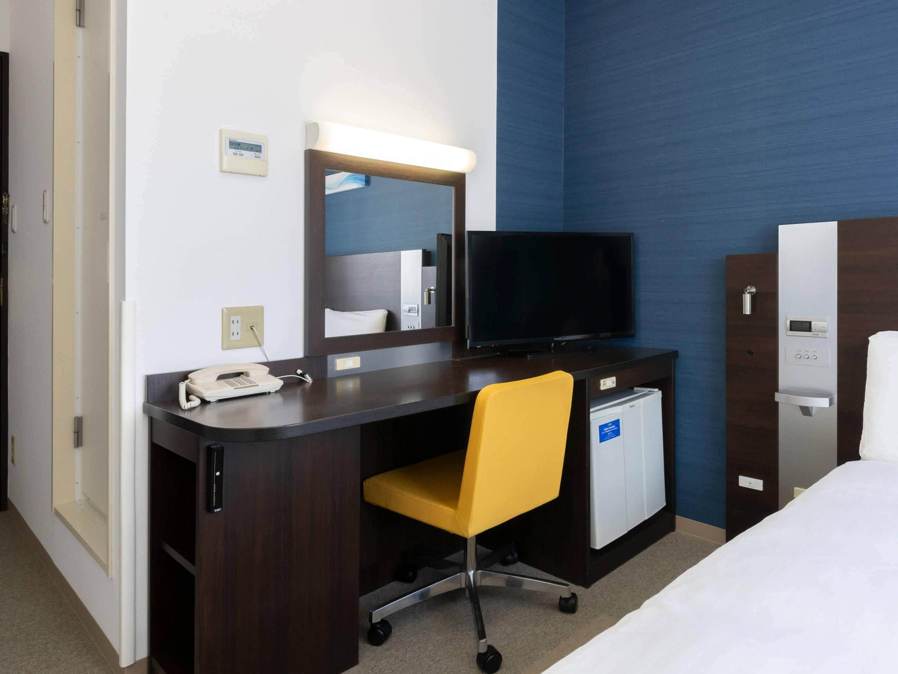 Una habitación de hotel con escritorio, silla, televisión, cama y minibar.