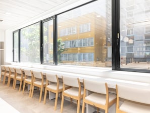A modern hotel interior with a long bench seating area, large windows, and a view of the building's exterior. - Comfort Hotel Yokohama Kannai (Yokohama)