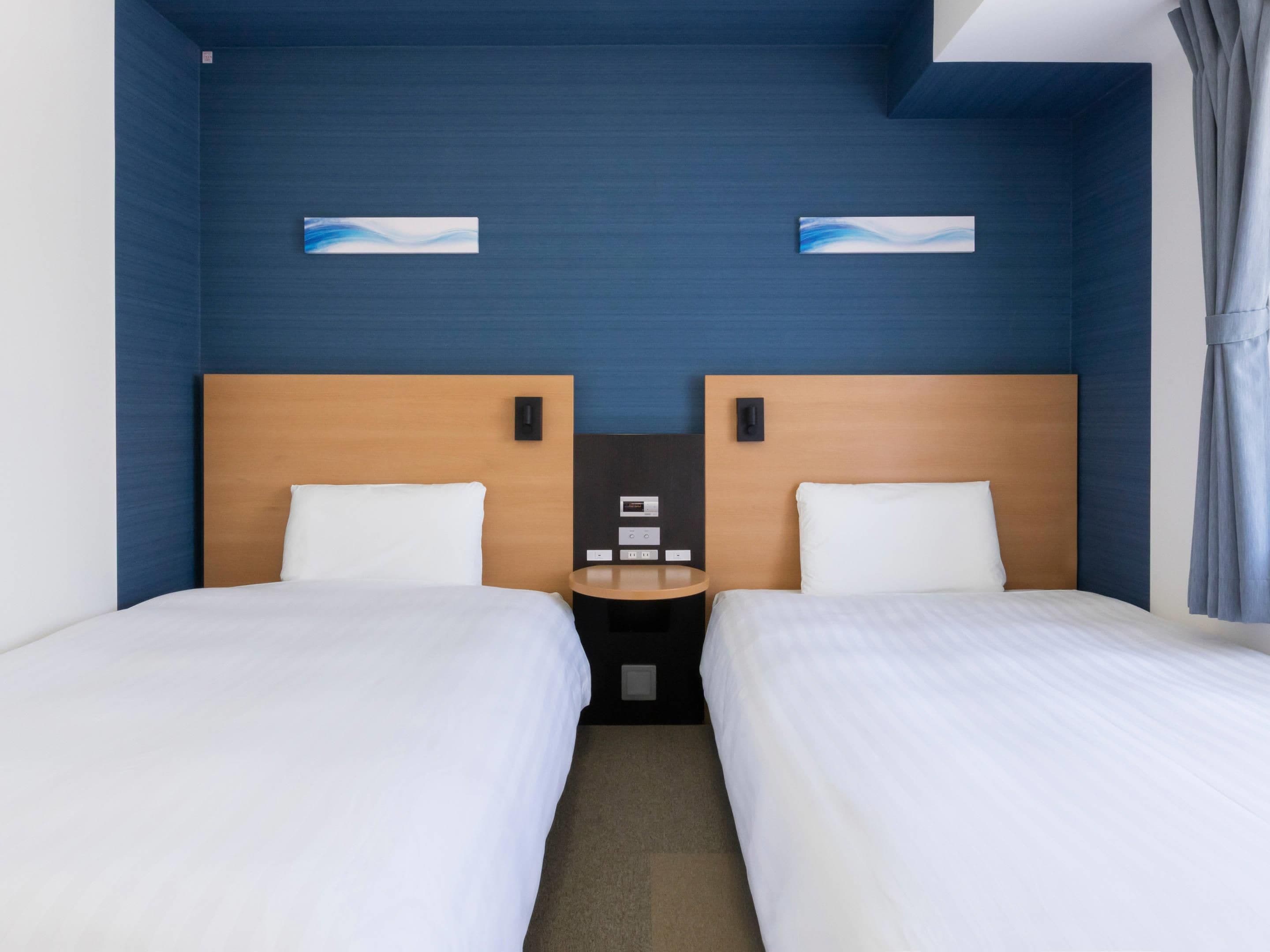 Habitación de hotel con dos camas, una mesita de noche y un panel de control en la pared.