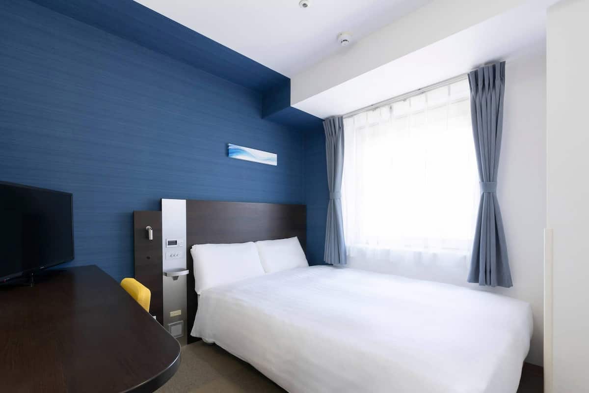 A hotel room with a large bed, a desk with a chair, a TV, and a window with curtains.