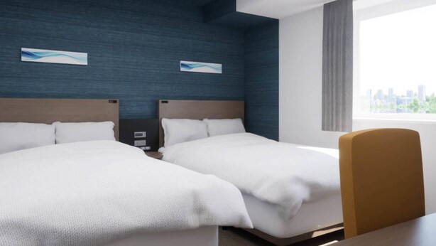 Hotellihuone, jossa on kaksi sänkyä, puinen pääty, työpöytä ja ikkuna, josta on näkymä kaupunkiin.