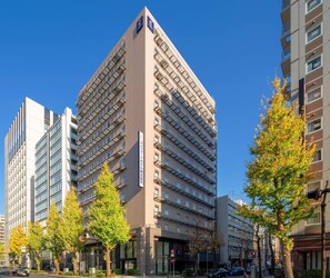 Um hotel com vários andares, design moderno, com uma entrada de canto imponente e várias varandas.