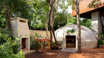 A wooden deck with a stone wall, a white dome structure, and lush greenery.