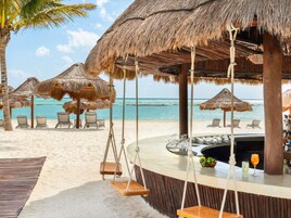 A beachside bar with thatched umbrellas, lounge chairs, and a view of the ocean.