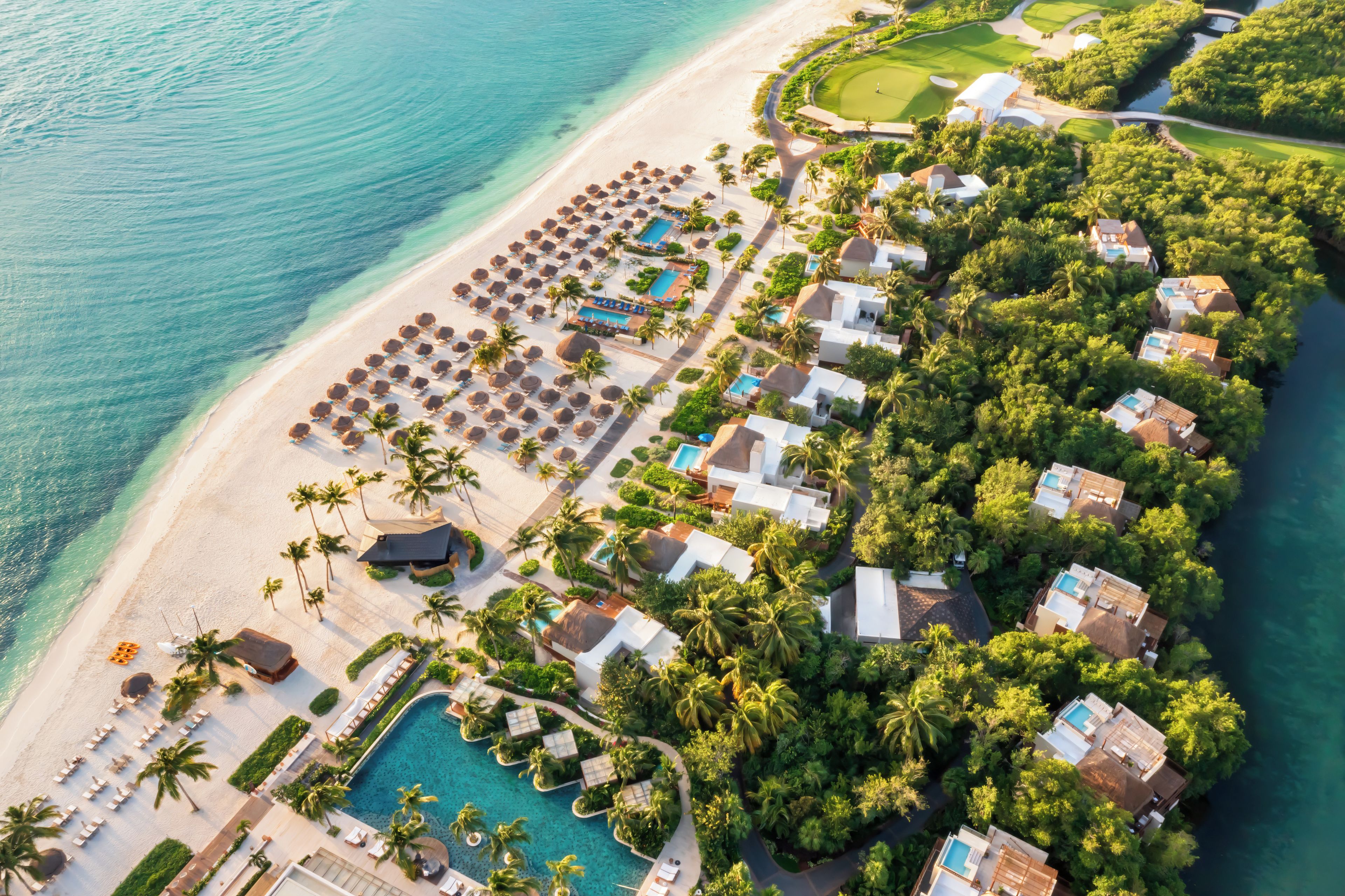 Eine Vogelperspektive zeigt ein Resort mit Strand, Poolbereich und üppiger Vegetation.