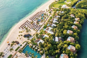 Vista aérea de un resort con playa, zona de piscina y exuberante vegetación.