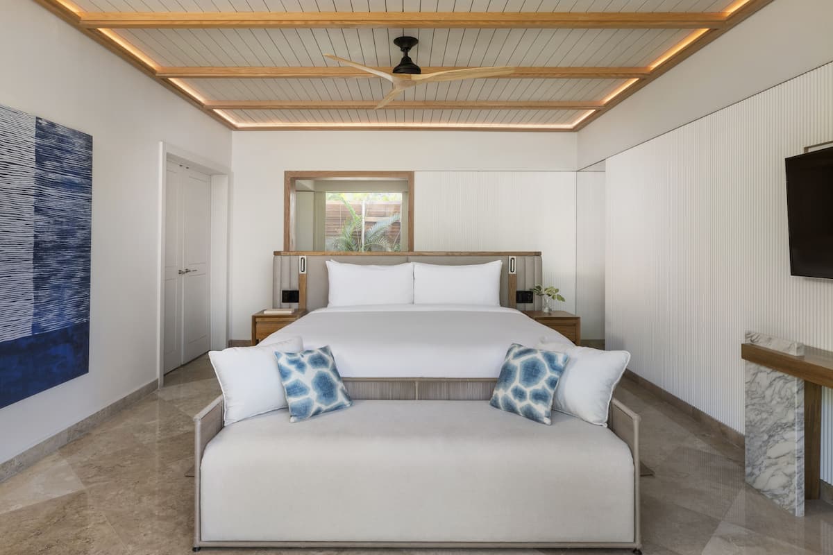 A modern bedroom with a large bed, a sofa, a ceiling fan, and a TV on the wall.