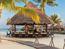 A beachside bar with thatched umbrellas, lounge chairs, and a wooden deck leading to the sand.