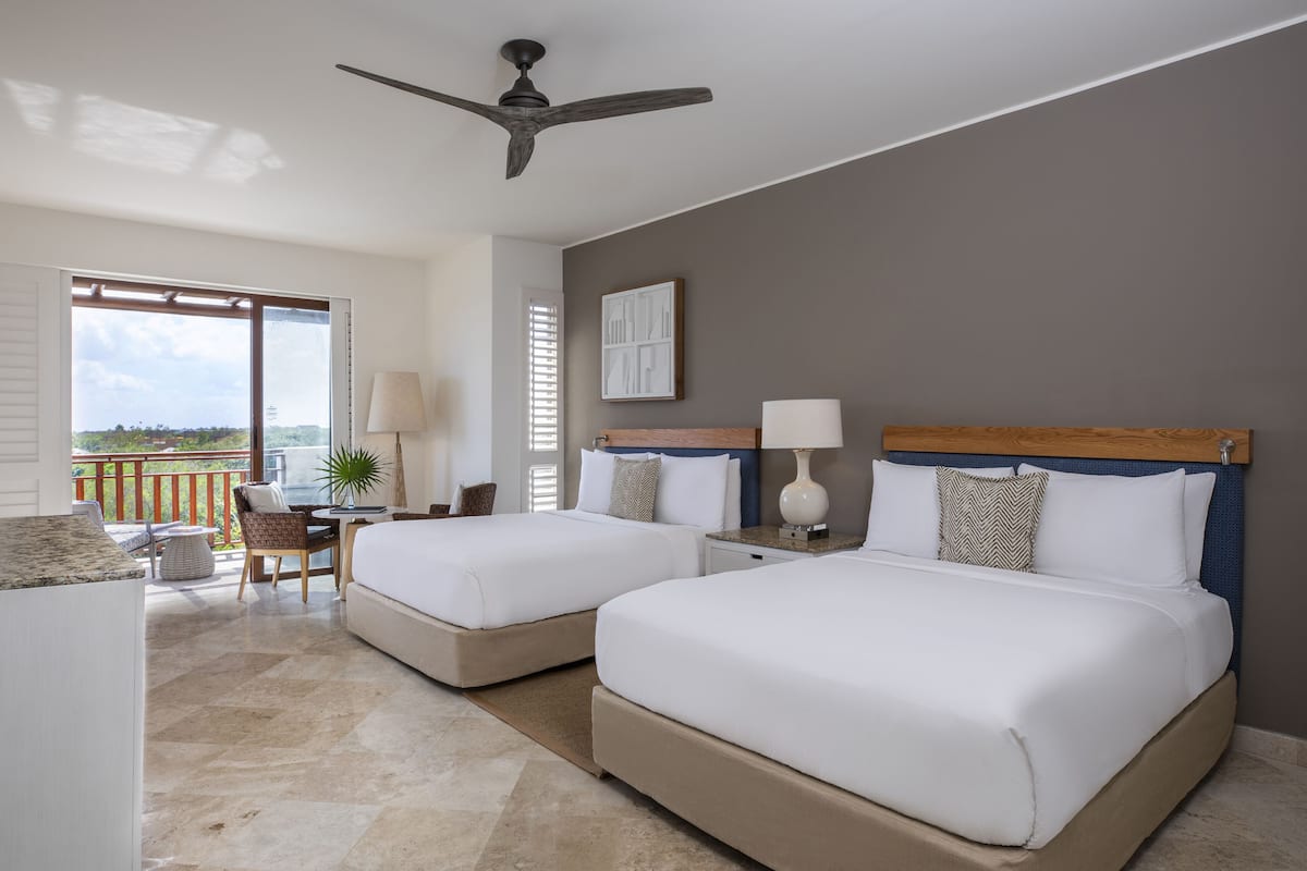 A hotel room with two beds, a balcony, a ceiling fan, and a view of the outdoors.