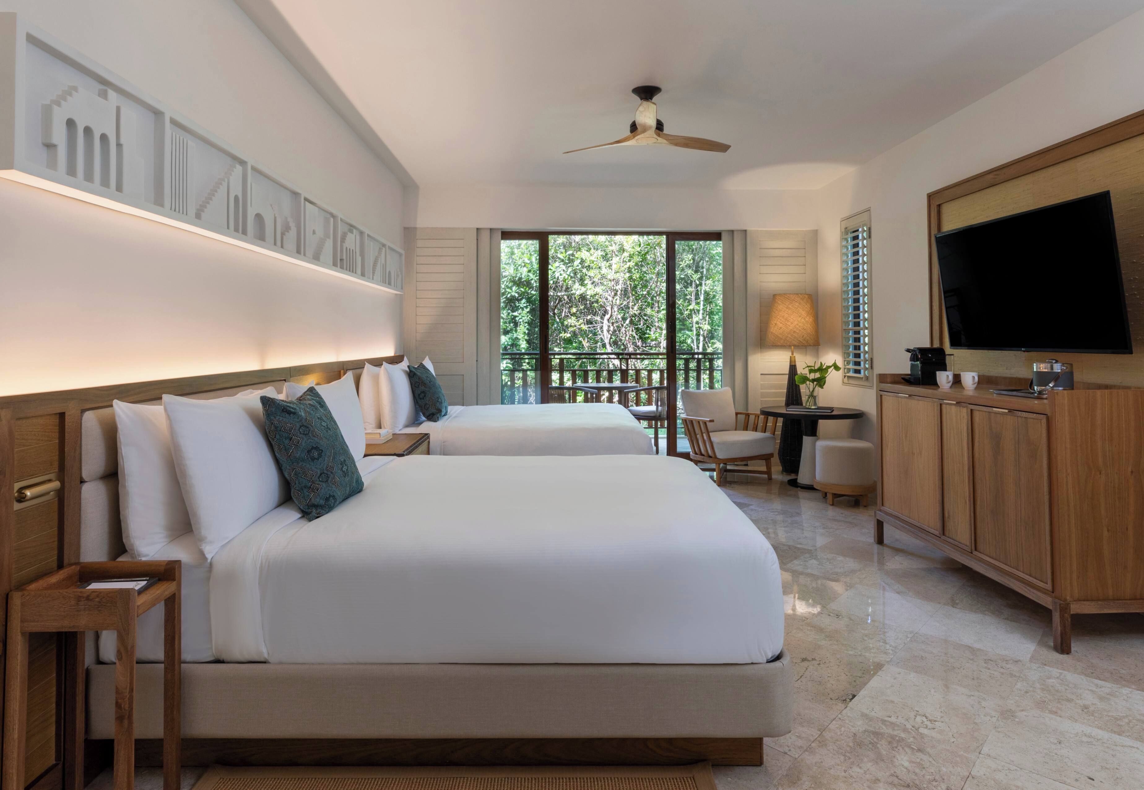 Habitación de hotel con una cama grande, un escritorio, una silla, un televisor y un balcón con vista a árboles.