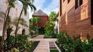 Un resort tropical con una estructura de techo de paja, un edificio de madera y un camino pavimentado bordeado de plantas tropicales.