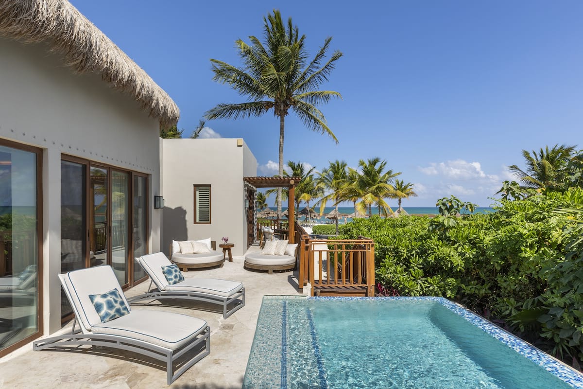 A poolside area with lounge chairs, a thatched-roof structure, and a view of the ocean.