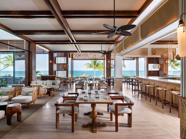Ein geräumiges Restaurant mit Holztischen, einer Bar und Blick aufs Meer.