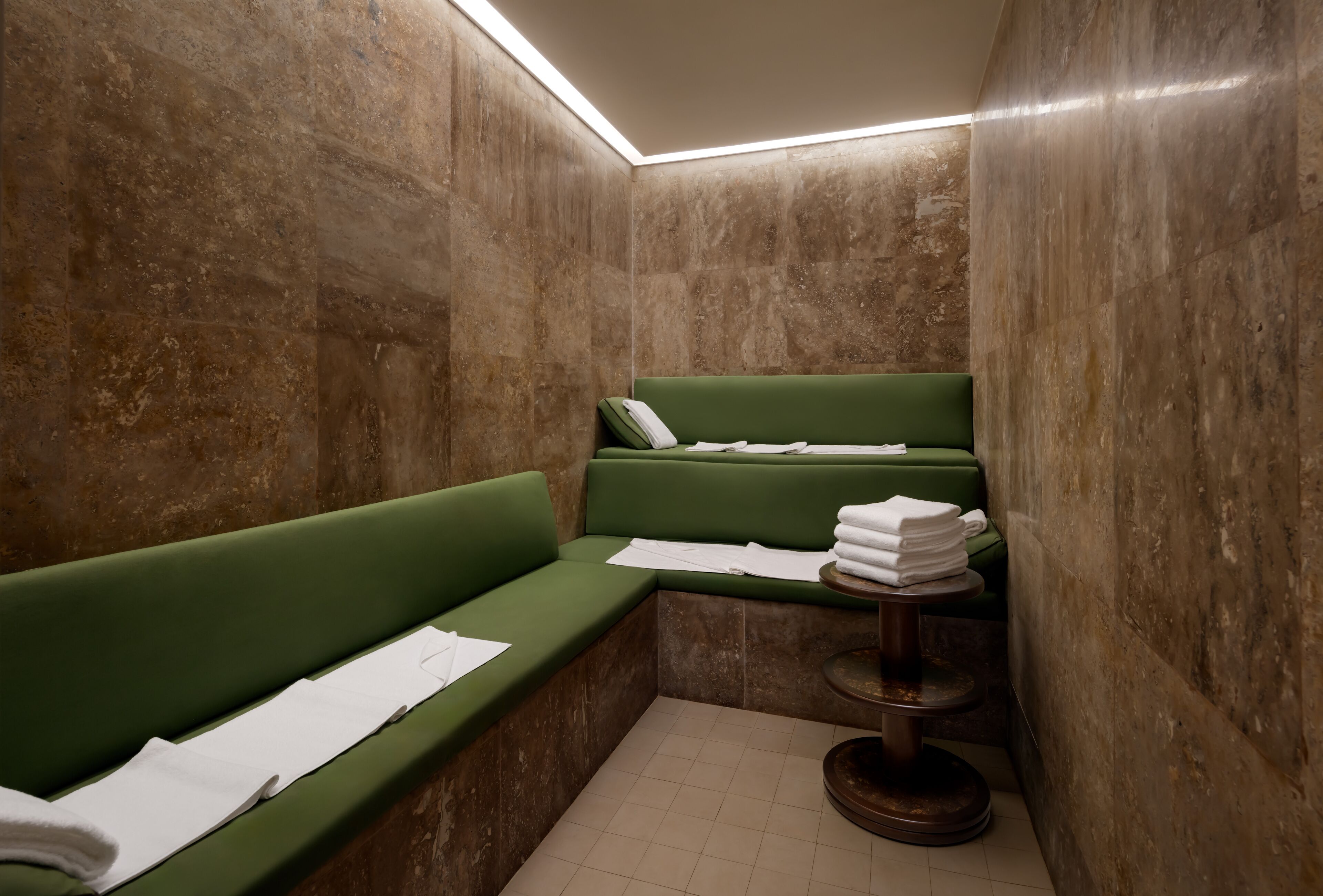 Un espacio pequeño y privado tipo spa con un banco acolchado verde, una mesita con toallas y un teléfono instalado en la pared.