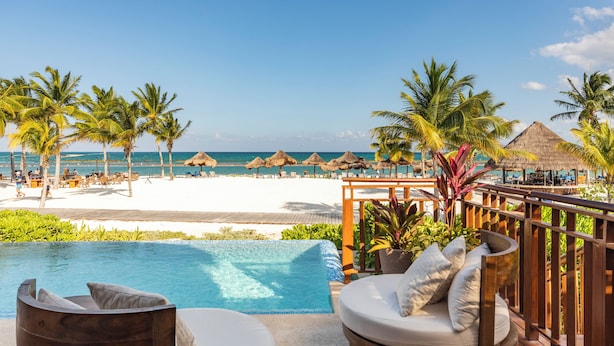 Un espace aménagé au bord de la piscine, avec vue sur la plage, des chaises longues et des parasols en chaume.