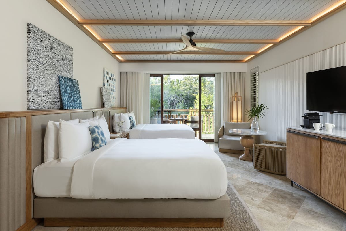 A modern hotel room with a large bed, a TV, a desk, and a balcony with a view of trees.