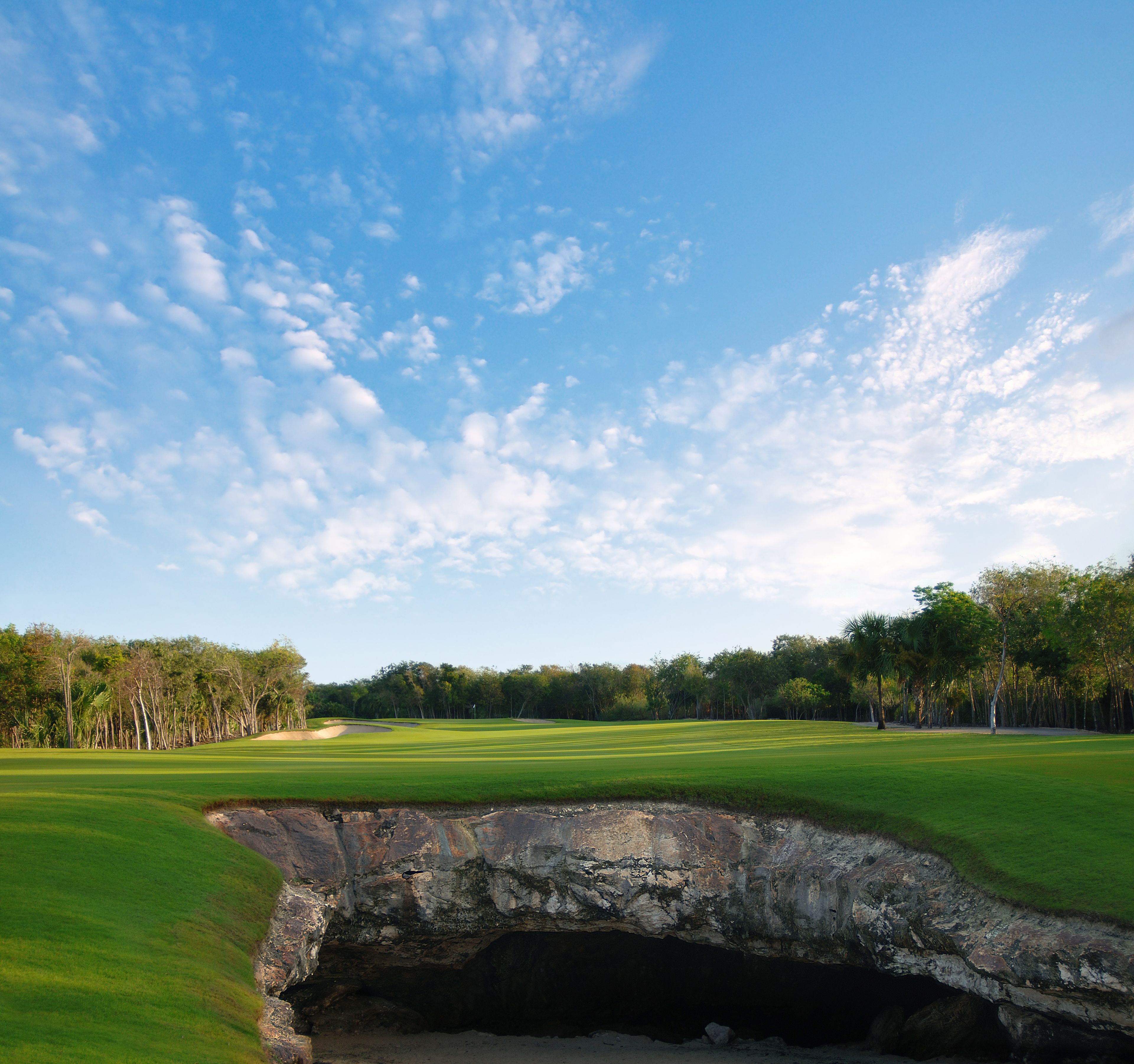 A golf course with a bunker, trees, and a clear sky.