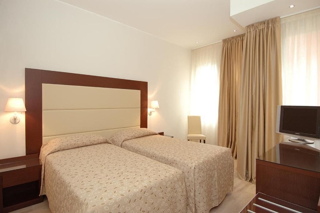 A hotel room with two beds, a TV, a desk, and a chair.