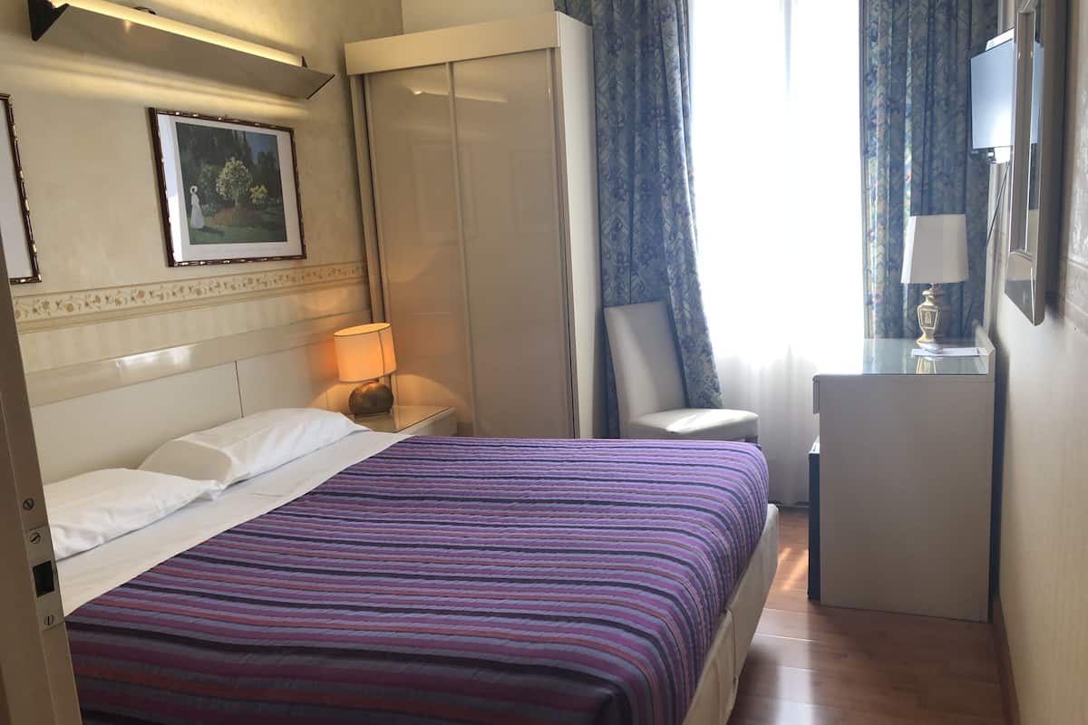 Une chambre d’hôtel avec un lit, un bureau, une chaise, une lampe et un tableau au mur.