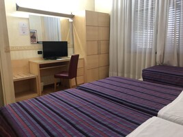 Camera d'albergo con scrivania, sedia, televisore, armadio e due letti.