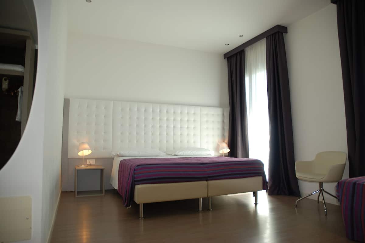 Une chambre à coucher moderne avec une tête de lit capitonnée, une table de chevet avec une lampe, un banc au pied du lit et une chaise.