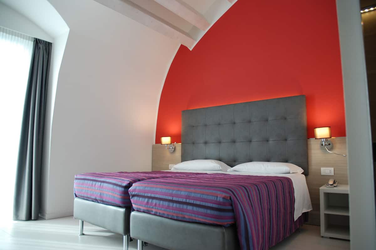 Une chambre d’hôtel moderne avec un grand lit, deux tables de chevet et un mur d’accent rouge.