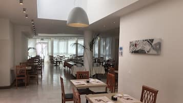 Un vaste espace dédié à la salle à manger, avec plusieurs tables et chaises, un grand lustre suspendu et, en arrière-plan, une vue sur l’ensemble de la salle à manger.