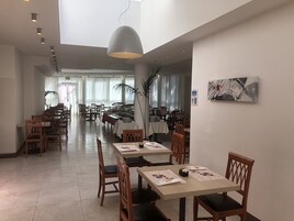 Un'ampia sala da pranzo con diversi tavoli e sedie, una grande lampada a sospensione e vista sulla sala da pranzo sullo sfondo.