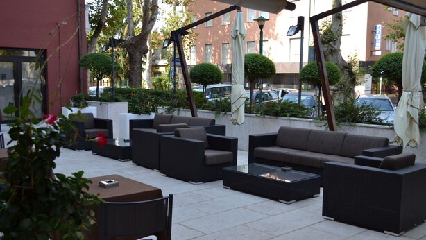 An outdoor seating area with sofas, chairs, and a table, surrounded by greenery and a city street. - Hotel Lugano Torretta (Mestre)
