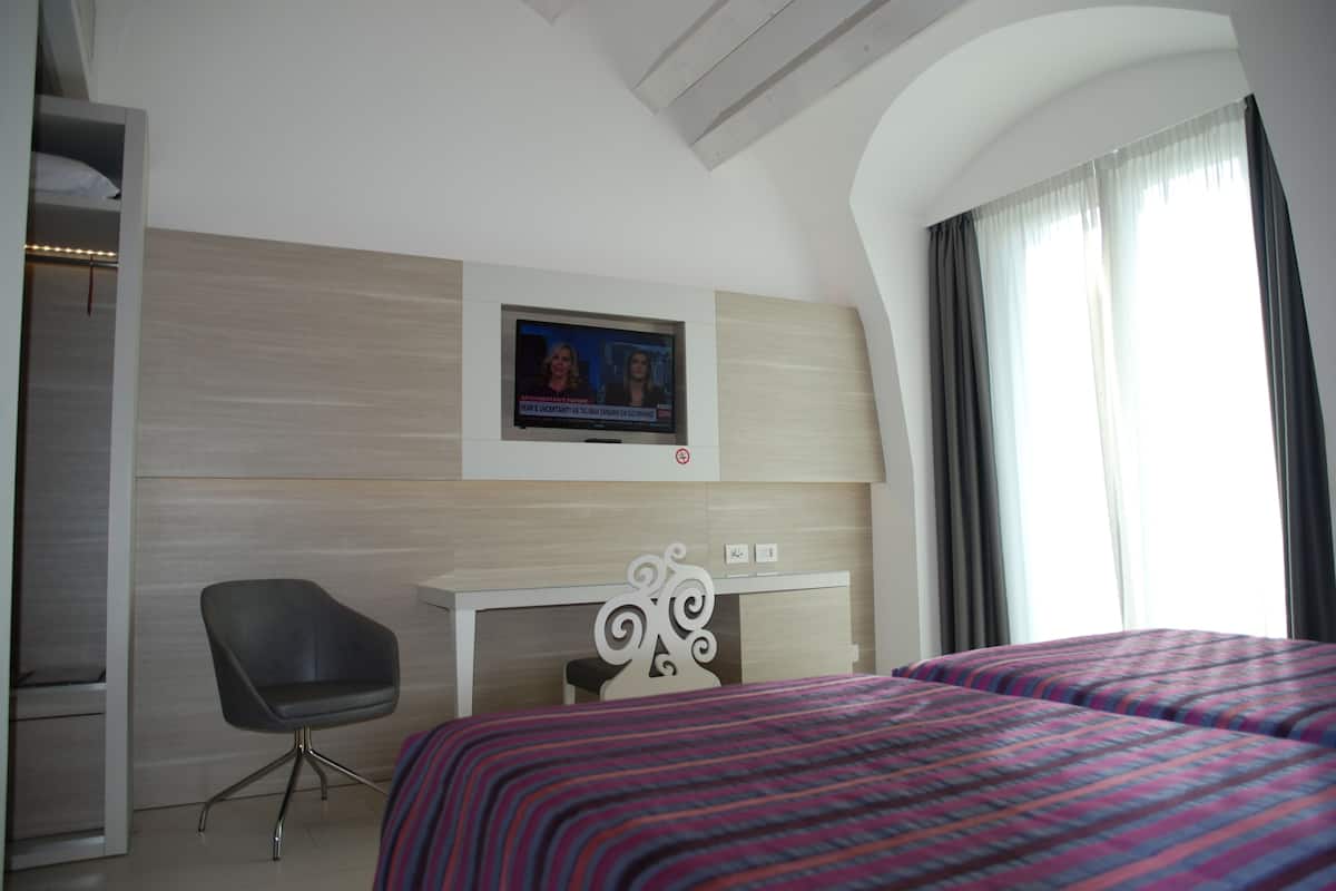 Une chambre d’hôtel équipée d’un lit, d’un bureau, d’une chaise et d’un téléviseur fixé au mur.