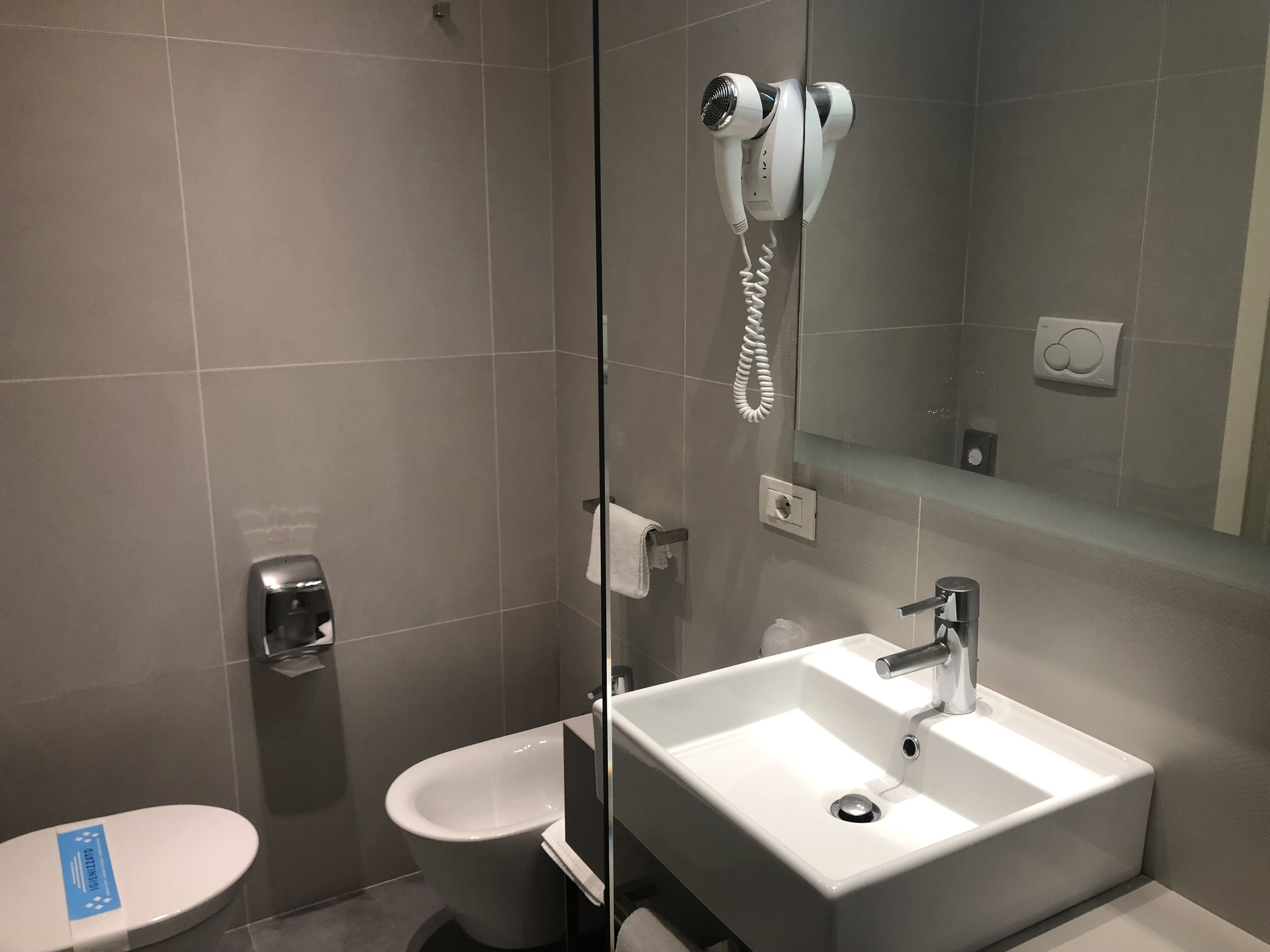 A modern bathroom with a large mirror, a white sink, and a handheld hair dryer mounted on the wall.
