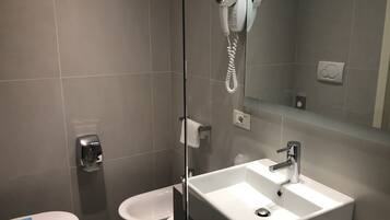 A modern bathroom with a large mirror, a white sink, and a handheld hair dryer mounted on the wall.